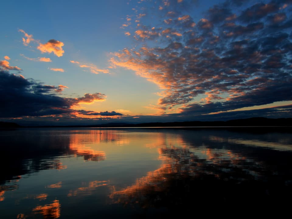 Wolkenreste leuchten in der Morgensonne und spiegeln sich im See.