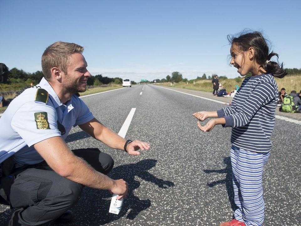 Ein Polizist kniet auf der Strasse und spielt mit einem Flüchtlingsmädchen