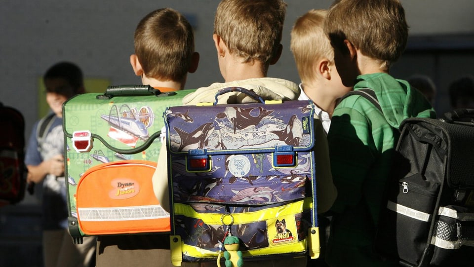 Kinder stehen in einer Gruppe, auf dem Rücken tragen sie Schulrucksäcke. 