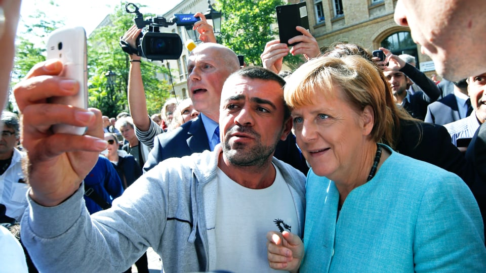 Angela Merkel posiert mit einem Mann vor dessen Smartphone.