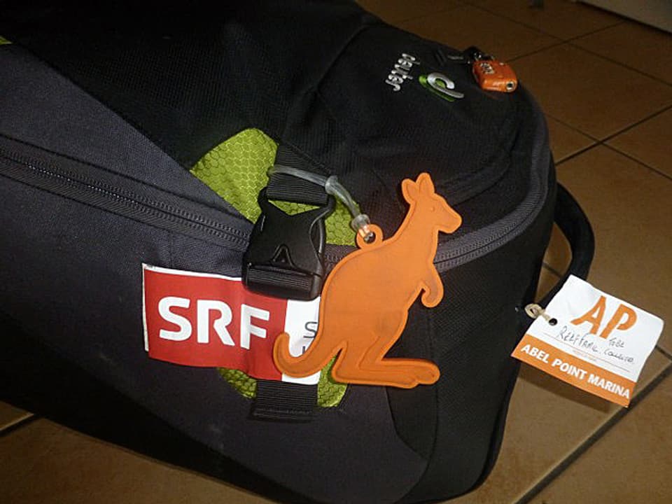 Schwarzer Rucksack mit SRF-Aufkleber und Känguru-Anhänger.