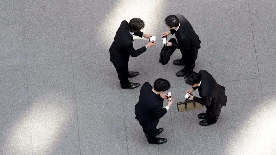Eine ausgefeilte Zeremonie Vier Geschäftsmänner in schwarzen Anzügen tauschen in Tokio ihre Visitenkarten.