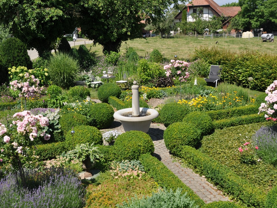 Ein grüner, gepflegter Garten mit Brunnen. 