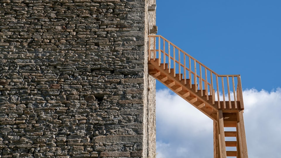Eine Holztreppe an der Fassade eines Steinturms.
