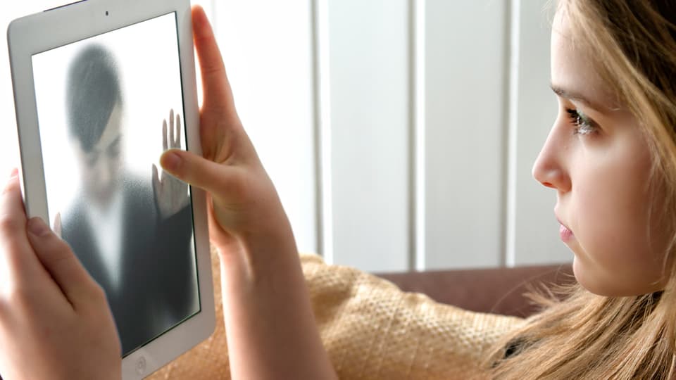 Eine junge Frau sieht auf dem Bildschirm eine andere Frau, die den Screen berührt.