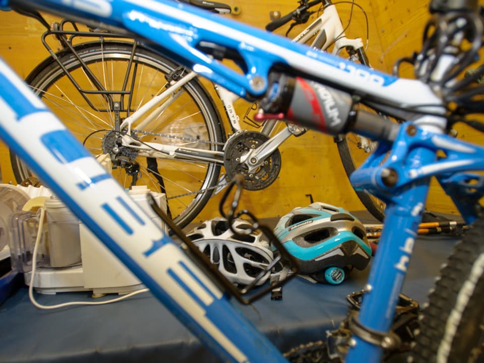 Ein blaues und ein weisses Fahrrad, dazu ein grauer und ein hellblauer Velohelm.