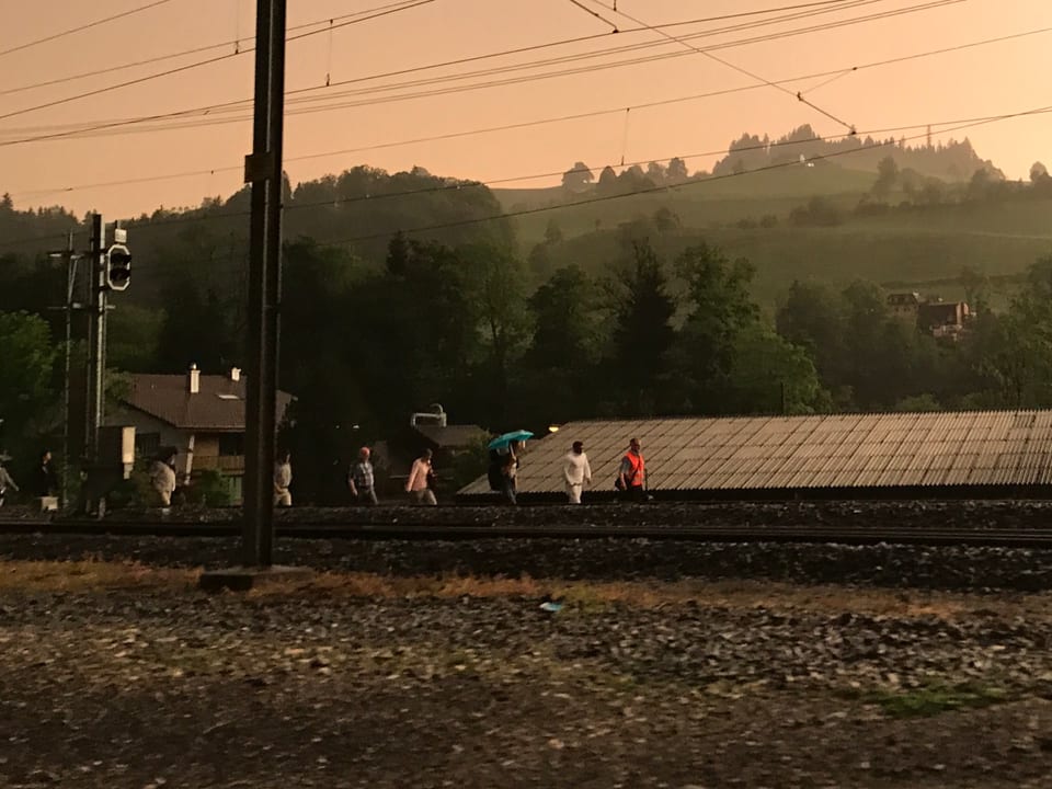 Menschen gehen neben dem Gleis, einer hält einen Schirm.