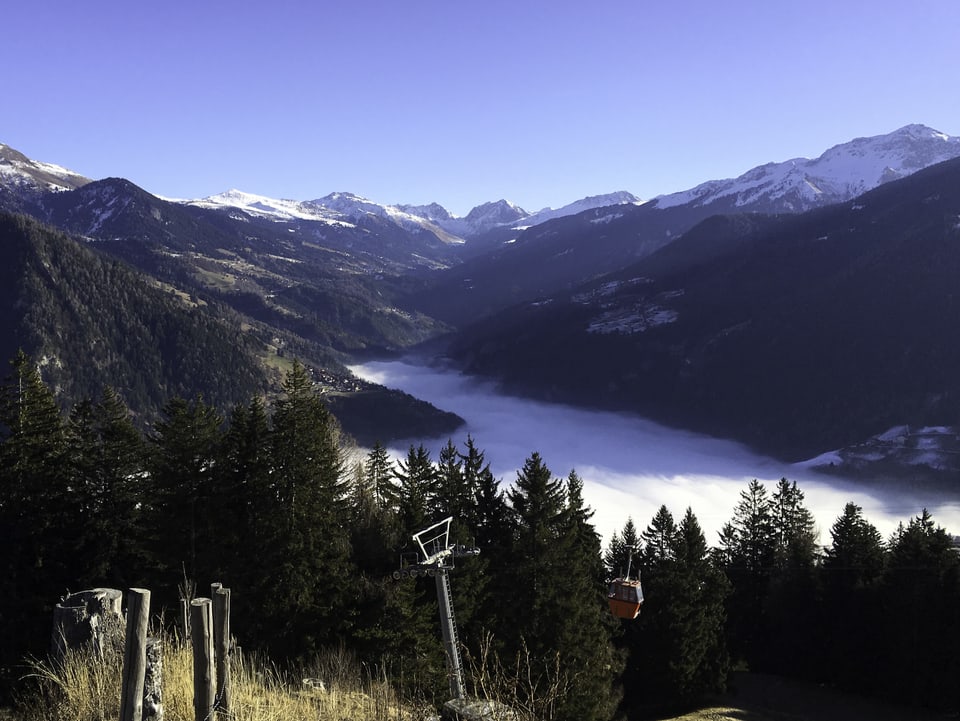 Blauer Himmel über den Alpen, im Tal unten liegt grauer, dichter Nebel.