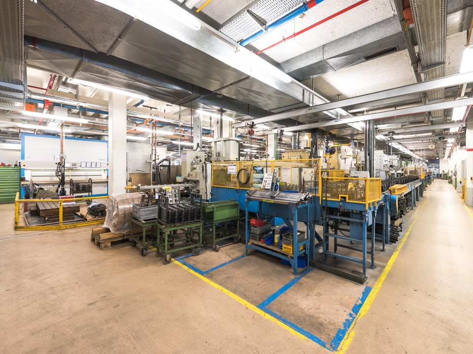 Blick in die Fabrikationshalle mit blauen Maschinen.