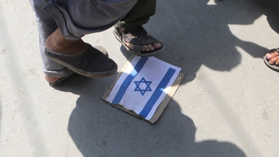 Füsse treten auf ein Bild der israelischen Flagge, das auf dem Boden liegt.