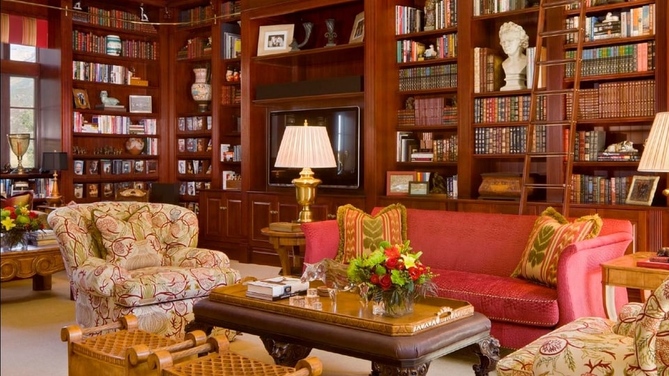 Ein Blick ins Wohnzimmer, das vor Büchern überquillt, die fein säuberlich in einer Bücherwand stehen. 
