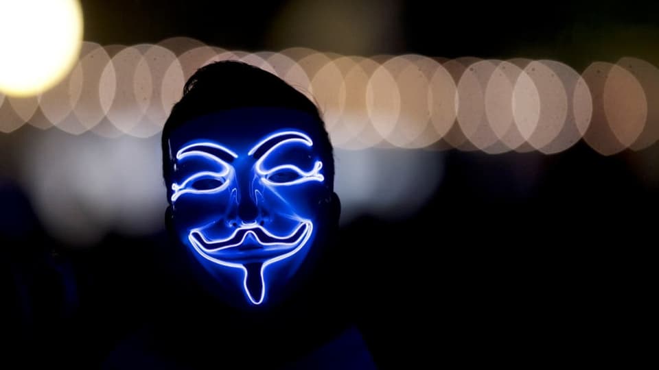 Person mit Anonymous-Maske, beleuchtet im Dunkeln