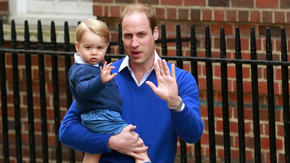 Prinz William trägt Prinz George. Beide winken in die Kamera.