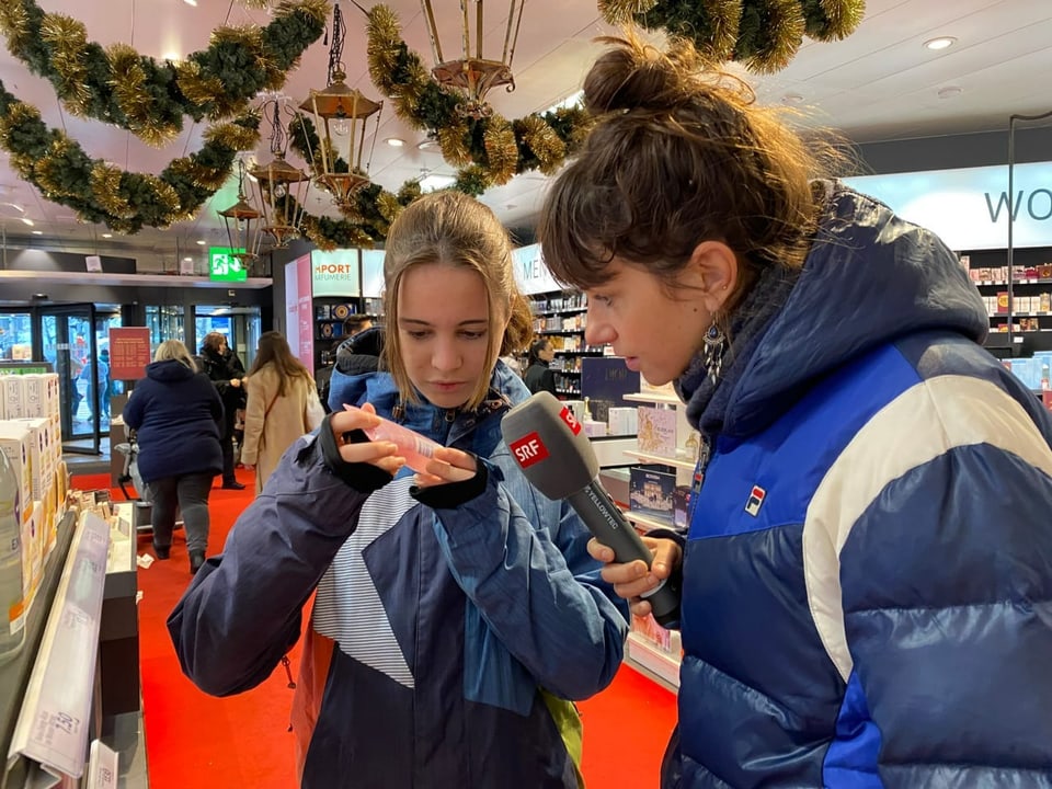 Die beiden Reporterinnen Dania und Zoe stehen vor in einem Einkaufsgeschäft in Zürich und schauen Kosmetikprodukte an.