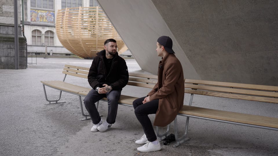 Livio und Fabian sitzen auf einer Bank und sprechen miteinander.