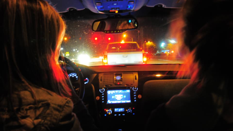 Zwei Frauen blicken im Dunkeln durch die Autoscheibe auf die dunkle Strasse.