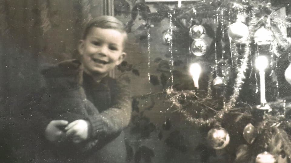 Das Bild zeigen einen jungen Buben vor einem Weihnachtsbaum.
