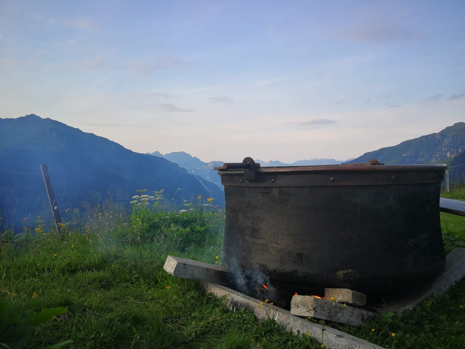 Ein Kochkessel über einem Feuer mit Ausblick in die Berge.