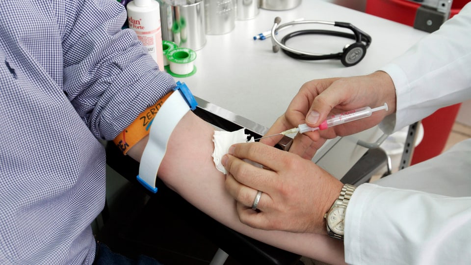 Ein Arzt nimmt einem Patienten mit einer Spritze Blut ab am Arm.