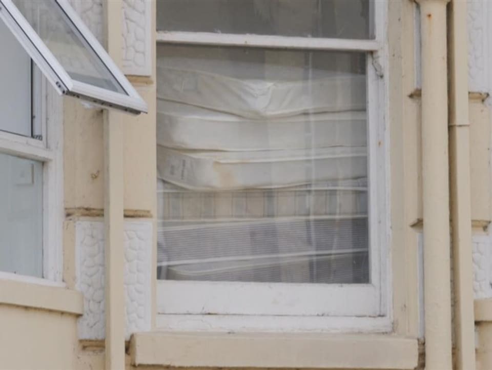Durch ein Fenster sieht man einen unordentlichen Stapel Matratzen