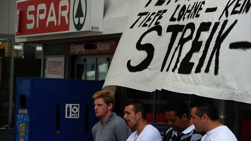 Mitarbeiter sitzen vor dem Spar-Laden, über ihnen ein Transparent mit der Aufschrift "Streik".