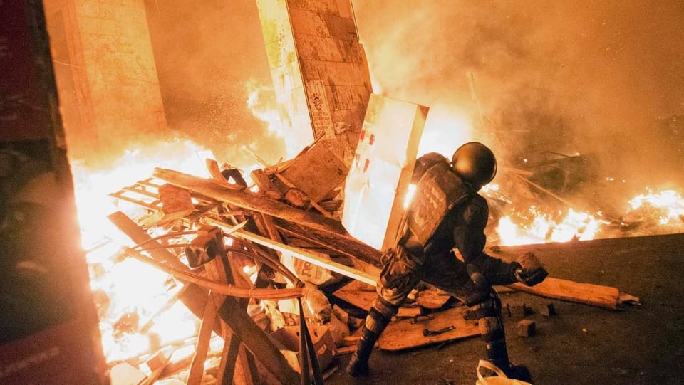 Ein Mensch in Kampfmontur steht an einer brennenden Barrikade. 