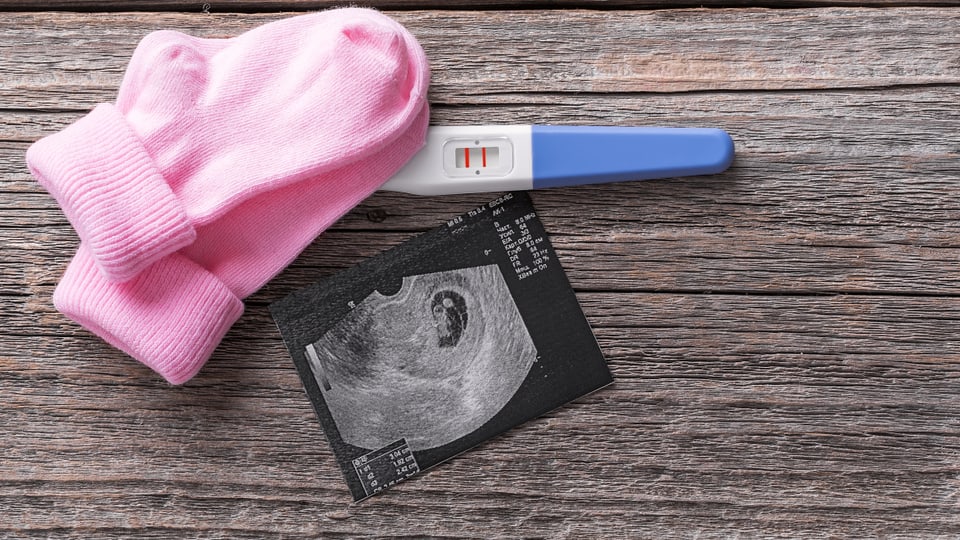 Rosa Babysocken liegen neben einem Schwangerschaftstest.