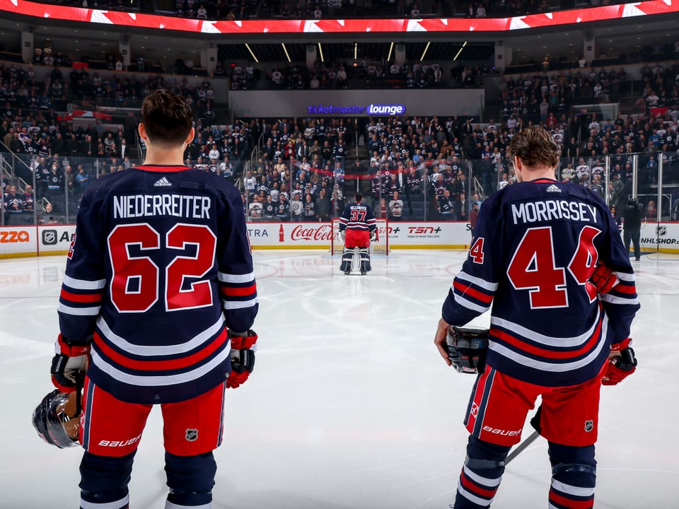 Zwei Eishockeyspieler von hinten betrachtet auf dem Eis vor einem vollen Stadion.