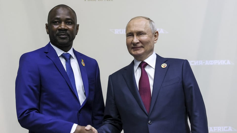 Assimi Goïta steht neben Wladimir Putin. Die beiden schütteln sich die Hand.