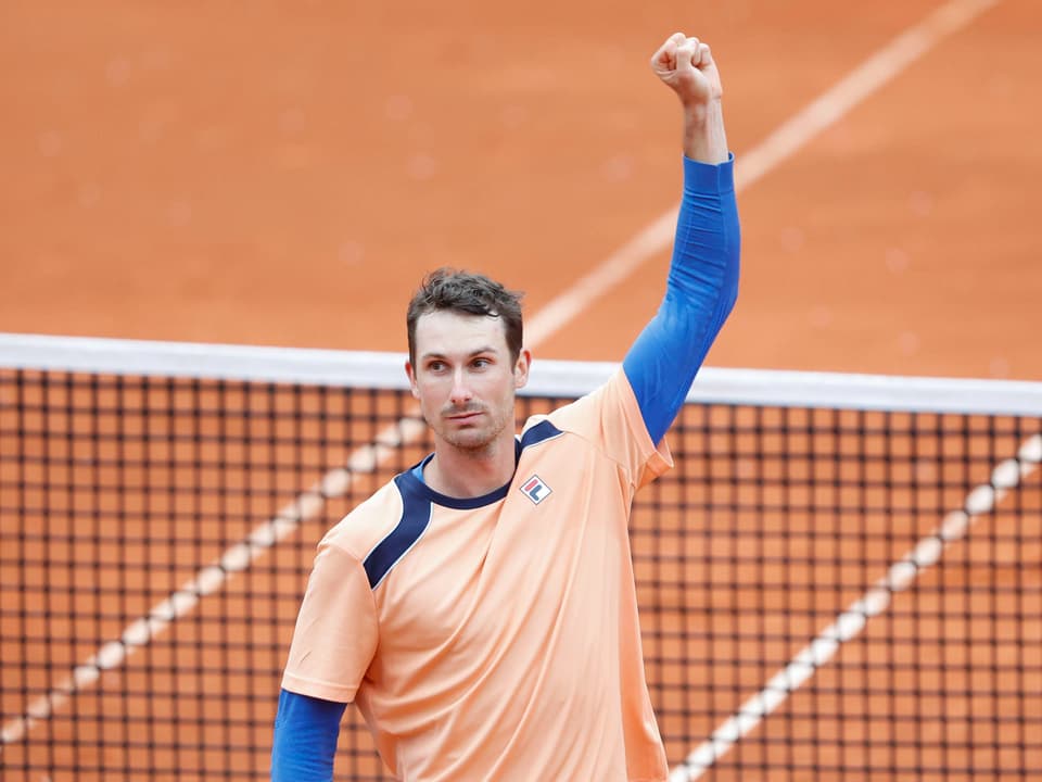 Tennisspieler mit erhobenem Arm feiert Sieg auf Sandplatz
