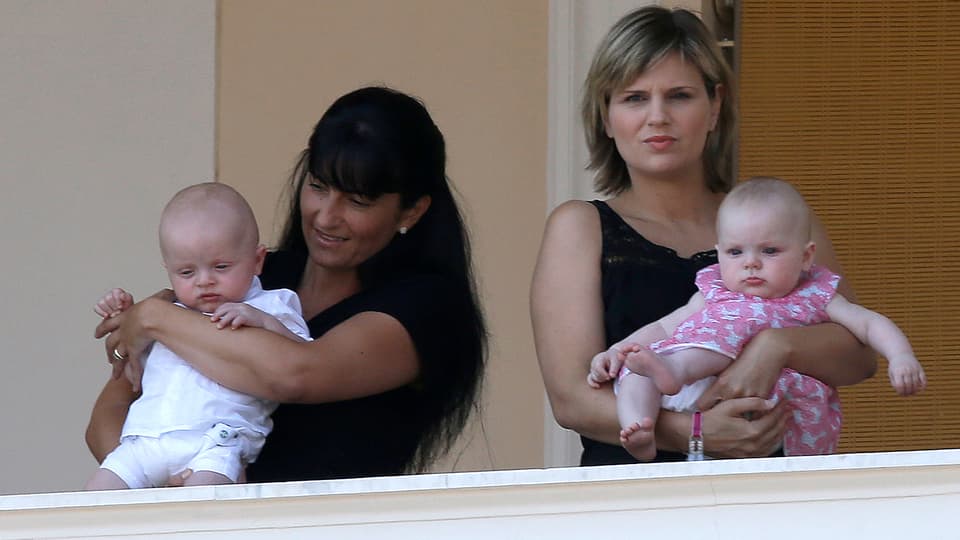 Zwei Nannys halten die Monaco Zwillinge. Links Jacques in weissen Stramplern und Shirt, rechts Gabriella im rosaroten Kleidchen.
