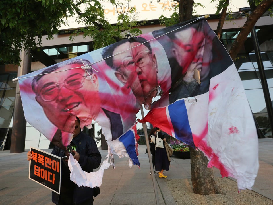 Banner mit rot besprayten Fotos von Nordkorea-Leadern.