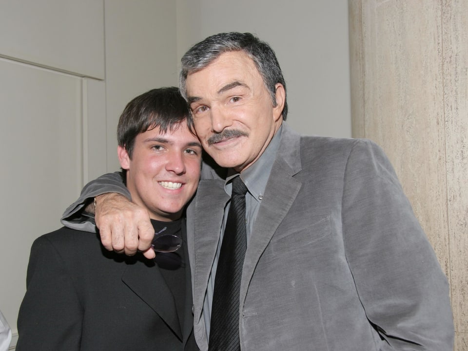 Burt Reynolds umarmt seinen Sohn und beide tragen einen Anzug. 