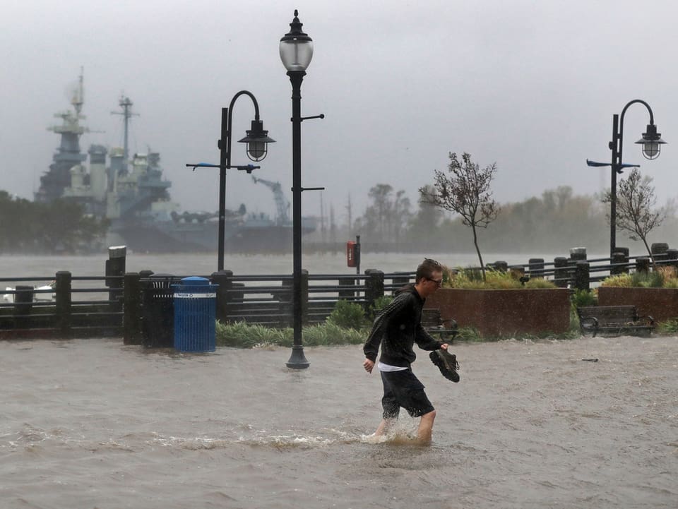Mann waatet durch überflutete Strasse.