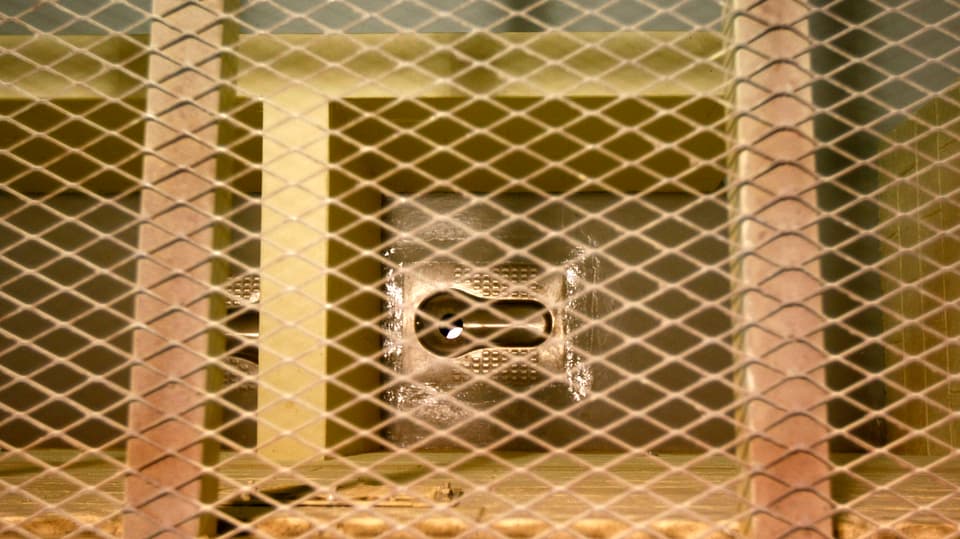 Offene Zellen-Latrine aus Metall von oben durch ein Gitter fotografiert.