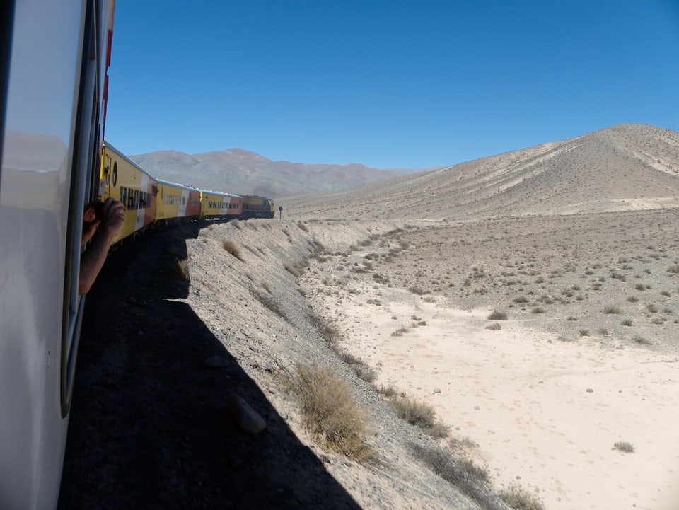 Blick aus dem Zugfenster auf die Lokomotive, die durch eine staubige Landschaft fährt.