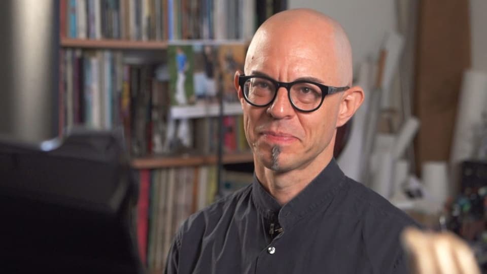 Ein Mann mit schwarzer Brille vor einer Bücherwand.