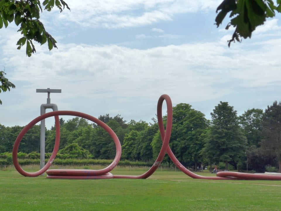 Skulptur eines überdimensionierten Wasserhahns mit rotem Schlauch