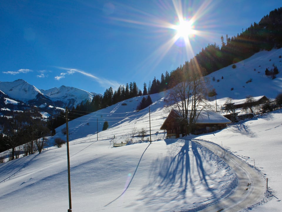 Der Blick in ein tief verschneites Bergtal. Am Hang steht ein Berner Bauernhaus. Die Sonne steht am blauen Himmel.