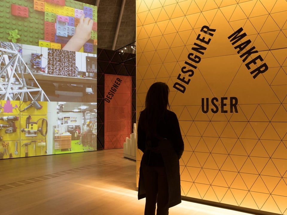 Eine Frau steht vor einer Museumswand, auf der steht "Designer, Maker, User".