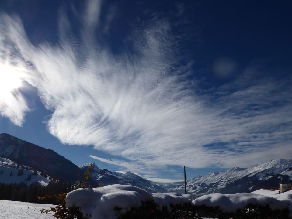 Der Blick ins verschneite Tal. Der Himmel ist blau mit weissen hohen Wolkenfeldern. Sie sehen aus wie ein grosses gewobenes Tuch.