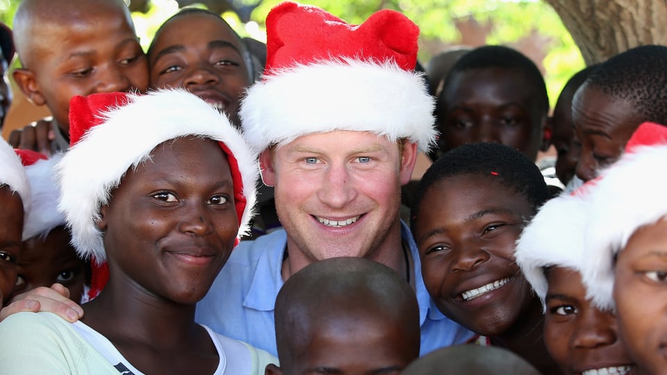 Prinz Harry trägt eine Nikolausmütze und wird umringt von Waisenkindern