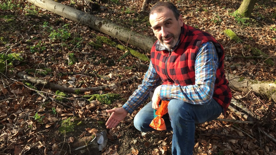 Marco Agostini sitzt im Wald und zeigt auf Abfall