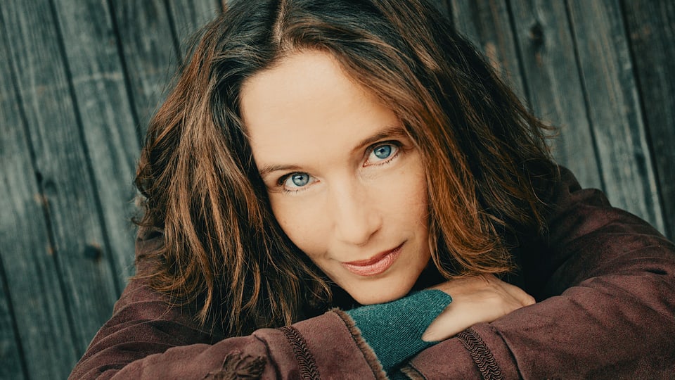 Eine Frau mit braunen Haaren und blauen Augen schaut in die Kamera. 