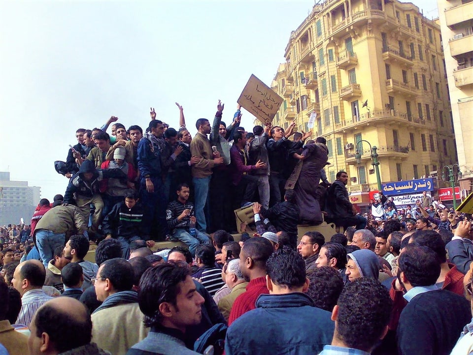 Eine Menschentraube sitzt und steht auf einem Militärlastwagen in Kairo auf dem Tahrirplatz.