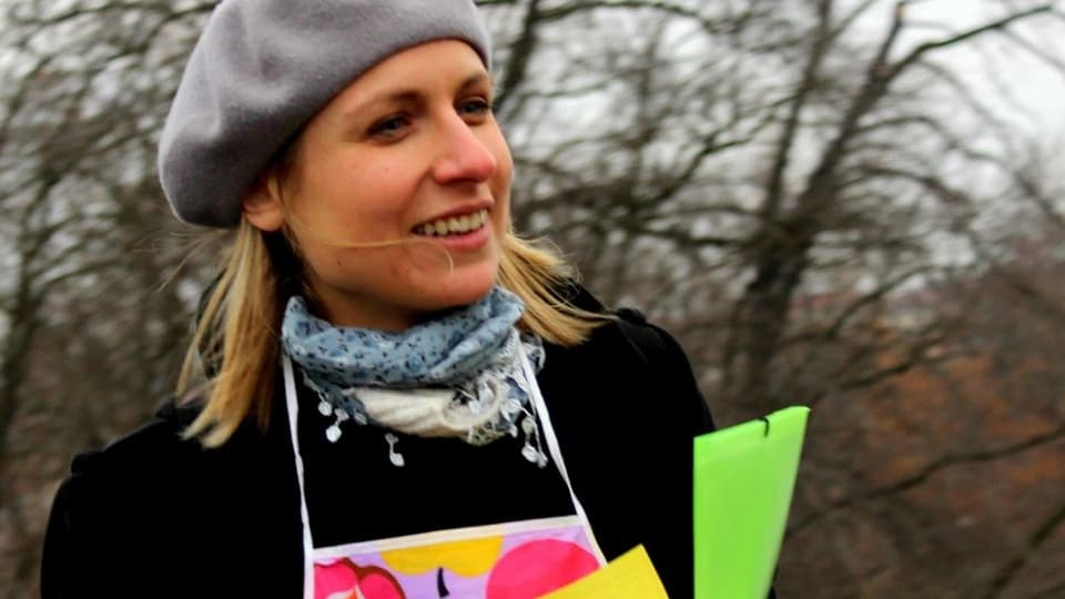 Olga Cieslarova, im Hintergrund kahle Bäume, sie hat farbige Zeedel in der Hand, die an der "Prager Fasnacht" verteilt wurden. 