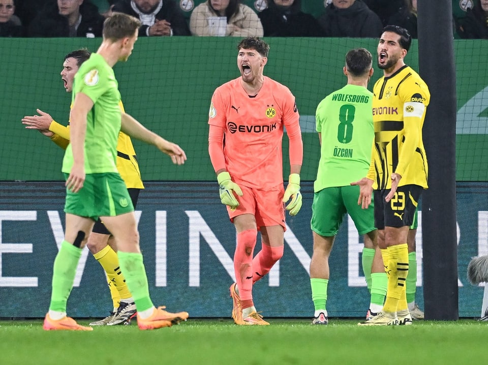 Jogadores de futebol em ação em campo, goleiro chamando.