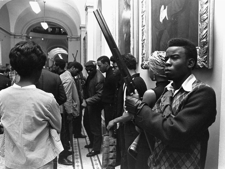 Schwarze Männer stehen bewaffnet an einer Wand.