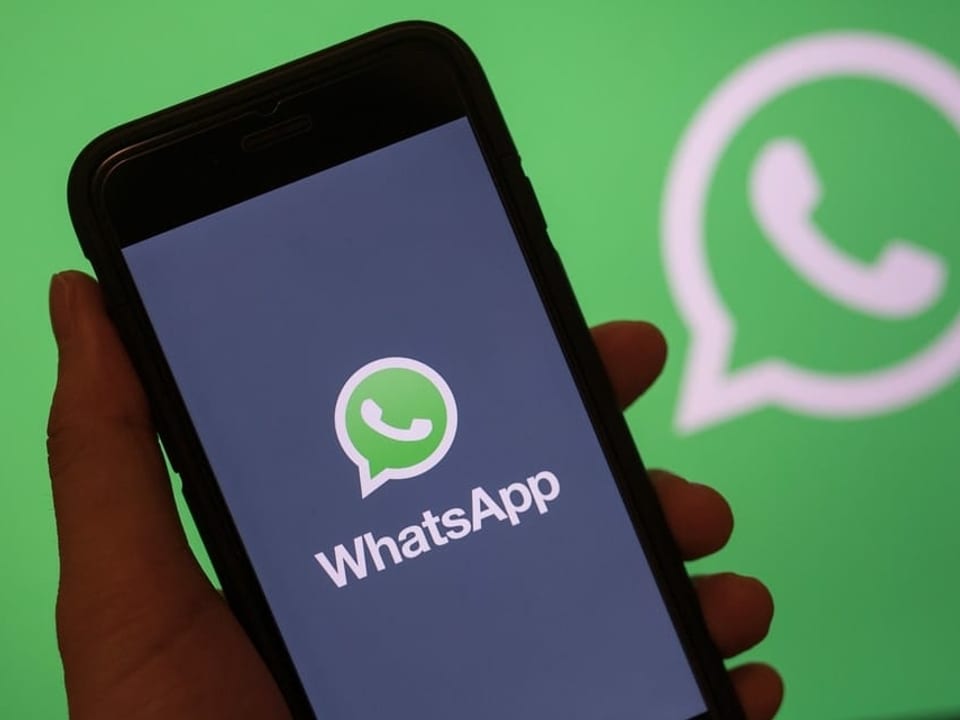 Hand hält Handy mit WhatsApp-Logo auf dem Display.