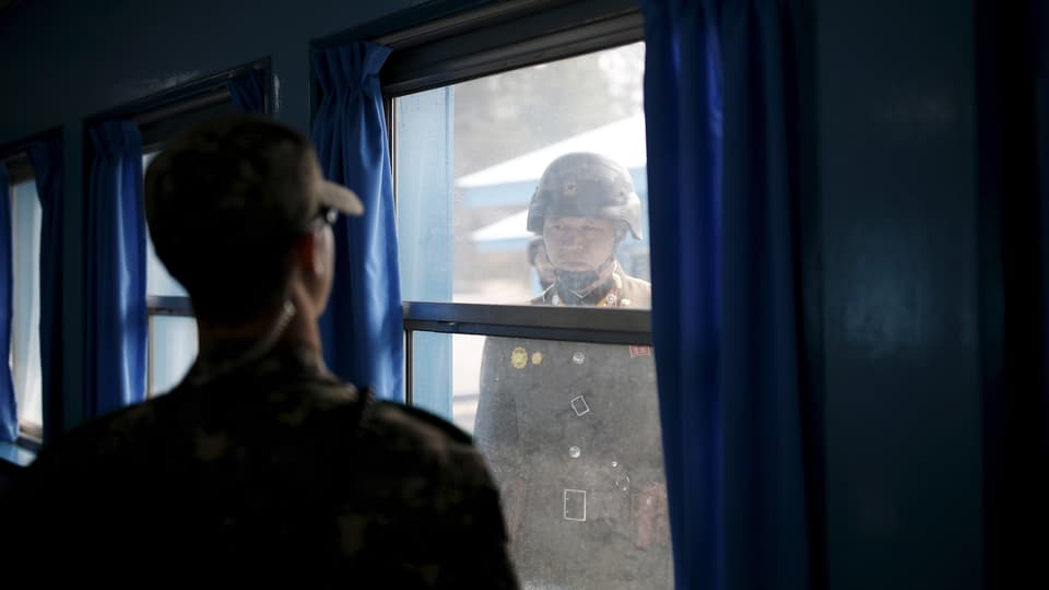 Nordkoreanischer Soldat blickt durch ein Fenster auf einen südkoreanischen Soldaten.